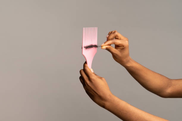 Mulher negra segurando pente com cabelo caindo depois de usar permanente capilar